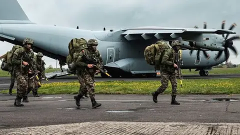 Crown 2023 Military personnel in uniform, carrying guns, walking alongside a plane.