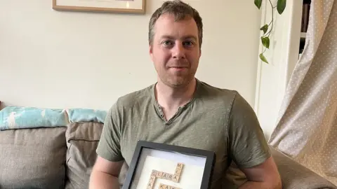 BBC A man holding a picture of names of his family