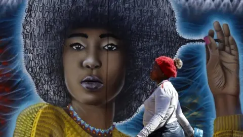 A woman walks past a spray-painted mural depicting a woman with an afro.