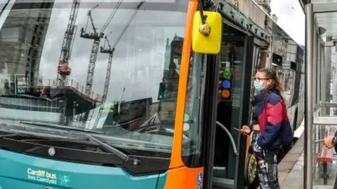 PA Media Passengers in masks getting on a bus in Cardiff