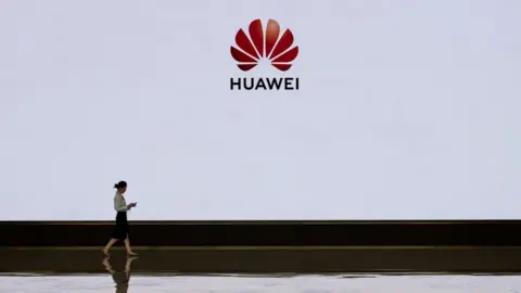 Getty Images A member of Huawei's reception staff walks in front of a large screen displaying the logo in the foyer of a building used for high profile customer visits and displays at the company's Bantian campus on April 12, 2019 in Shenzhen, China.