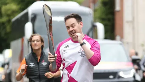 Getty Images Baton bearer Chris Luck holds the Queen's Baton during the Birmingham 2022 Queen's Baton Relay on a visit to Kenilworth