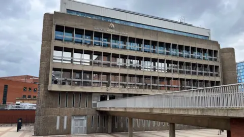 A brutalist stone multi-storey building, attached to a bridge. The words 'Sheffield Magistrates Court' can just about be discerned at the top of the building.