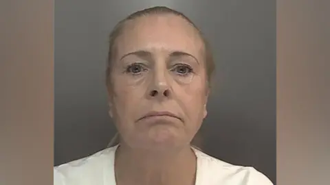 A police custody photograph of Helen Spree who has blonde hair, pulled back in a pony tail, and blue eyes. She is wearing a white t-shirt