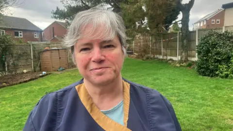 Photograph of Angela Goodman from Hollingworth. The image shows the 51 year-old in the garden of her home, where she runs her Prestige Dog Grooming business.