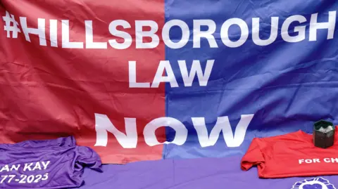 PA Media A close-up of a flag which says Hillsborough Law now