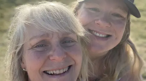 Family photo Jackie and Georgie, both with blonde hair, smile at the camera. Georgie, on the right, wears a baseball cap