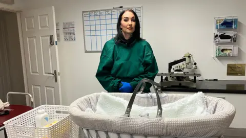 BBC/Naj Modak Evie Mawdsley at the mortuary at Rushton Family Funerals. In front of her is a Moses basket.