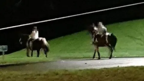 Supplied Two children on ponies on a street at night