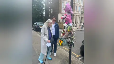 Two women are standing by the tide lamp which is covered in the roof of flowers