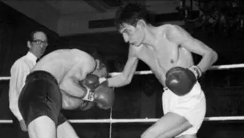 PA Media Two boxers fighting, one on the right in white shorts and on the left in black shorts