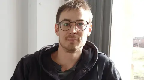 Forward Leeds A man with brown hair and glasses wearing a dark hooded jacket. 