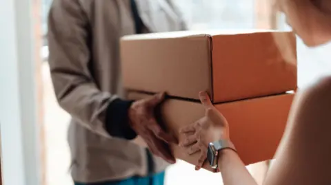 Cropped shot of courier person standing at front door, handing over a parcel to customer.
