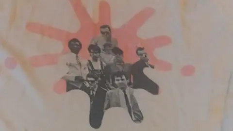 John Bassett A t-shirt which features a black and white print of The Blockheads. Part of the graphic is missing on one of the band members', after it was chewed and damaged by a dog.