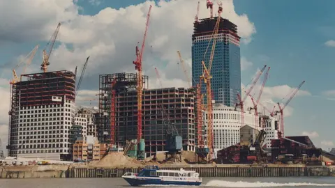 Getty Images The docks from the water, showing skyscrapers being built. There are lots of cranes and a boat on the river