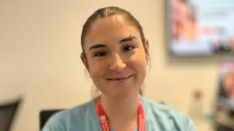 Trudie is wearing a blue t shirt and red lanyard against a blurred background 