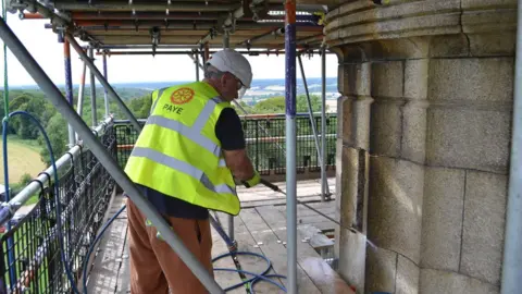 National Trust Workers wearing high vis and helmets on top of the Ashridge Monument begin cleaning work