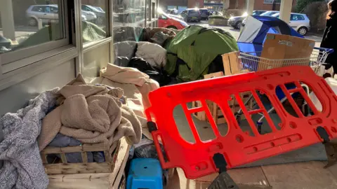 Blankets, wooden baskets, a shopping trolley and plastic fencing in a pile