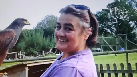 Bernadette smiling at the camera. She is holding a bird of prey on her right arm. She has a pair of sunglasses on her head. 