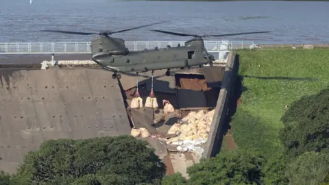 PA Media Chinook drops ballast at dam on Whaley Bridge reservoir in 2019 following storms that breached the lake wall