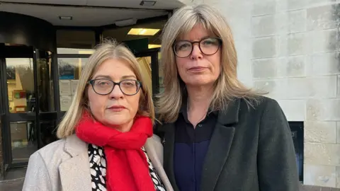 Fiona Elias, left, and Liz Hopkin. They both have spectacles and blond hair. Ms Elias has a beige jacket and red scarf. Ms Hopkin has a dark jacket with a blue and black top beneath it. 