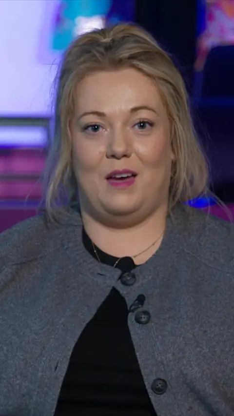 Nuala Moore has her hair tied up and is wearing a grey cardigan over a black tshirt. 