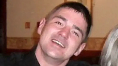 Police Scotland A man with short brown hair wearing a black top smiles at the camera. 