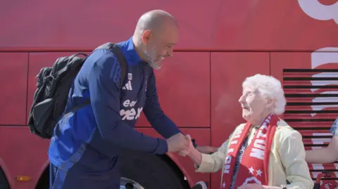 Nottingham Forest A man in a tracksuit smiles and shakes the hand of an older lady in red Forest scarf