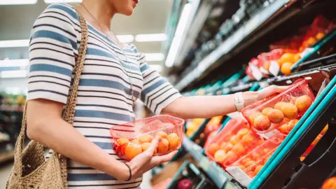A woman in a stripey top inside a supermarket looking at fruit and picking up nectarines