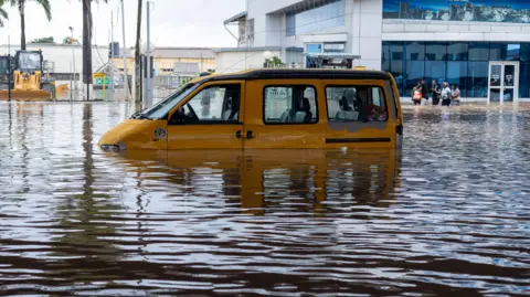 A yellow van half-submerged in floodwater