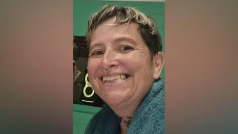 Contributed The woman is smiling and looking at the camera. She has a pixie cut hair style and facial piercings. She has a blue towel around her shoulders. 