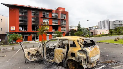  EPA-EFE/REX/Shutterstock A car burns and a building is gutted near Nouméa, New Caledonia. Photo: May 22, 2024