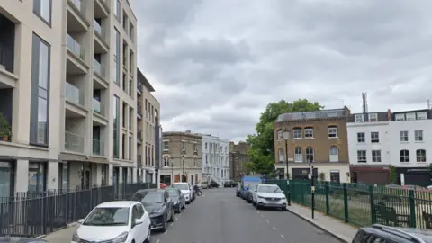 Google A street view of Faraday Road, with a modern block of flats on the left and a park and play area on the rights, with cafes on the corners of a crossroads visible in the distance