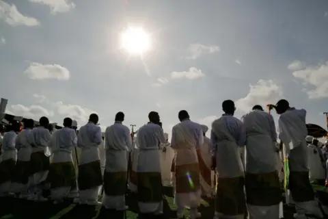 EPA An image taken from behind of Ethiopian Orthodox Christians celebrating Timket - they are wearing their traditional religious clothes. The bright sun can be seen in the sky above.