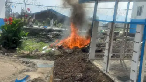 Health workers in Bisengimana can see a man in the background and their hands on the hips as he staring at a fire burning outside the Bisengimana Hospital in Goma after it was looted last month