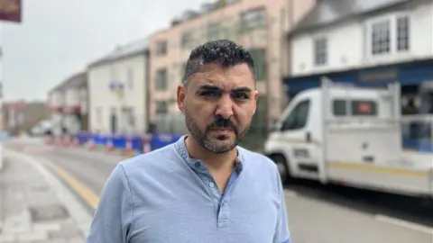 A business owner standing in front of the scaffolding which is three storeys tall.