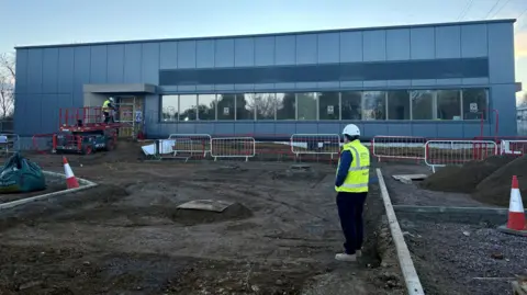 West Northamptonshire Council A man in a high-visibility jacket surveys the scene of the mortuary, which is a modern two-storey blue-cladded building.