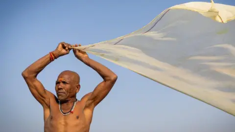 Reuters Image shows a Hindu devotee drying his cloth after taking a holy dip at Sangam, the confluence of the Ganges and Yamuna rivers with the mythical, invisible Saraswati river, during the "Maha Kumbh Mela", or the Great Pitcher Festival, in Prayagraj, India, 28 January, 2025