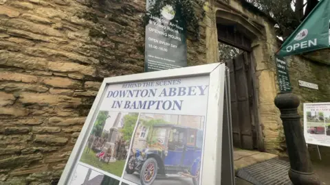 A sign outside a Cotswold stone building saying 'Downton Abbey in Bampton'.