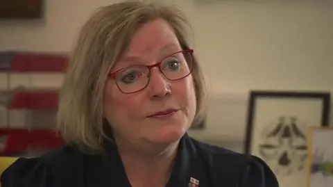 A woman in a black shirt with red glasses looking at the camera.