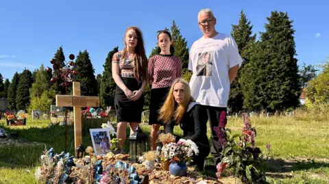 Vlad's family, Mia, Masha, Anna & Graham at his graveside in Southampton which is covered in tributes and marked by a home made wooden cross with his name on