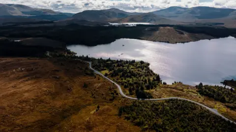 Red On Sports An overhead view of a road wending its way through countryside and round a loch