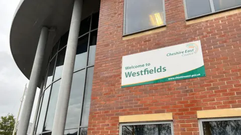 Close up of a sign saying welcome to Westfields on the side of the brick and glass-fronted building