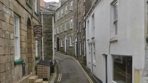 Google Street View image of Polkirt Hill in Mevagissey. It is a narrow single-lane road with double yellow lines on either side. Buildings line the road on both sides.