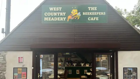 Exterior of the Beekeepers Cafe in Redhill, Bristol. Owner Rod Jenkins visible through open front doors. 