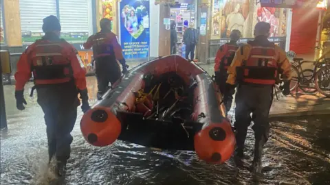 London Fire Brigade Firefighters carry a rescue dinghy through flood water in Blackheath