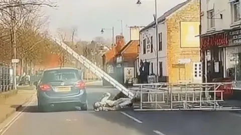 Scaffolding falling into the road and hitting a passing car.