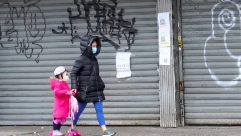 Getty Images people in masks walk past closed stores