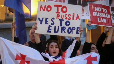 Reuters Protesters in Georgia hold signs in protest at the draft bill on foreign agents