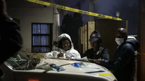 BBC/Shiraaz Mohamed Police taking notes at a crime scene in Lenasia